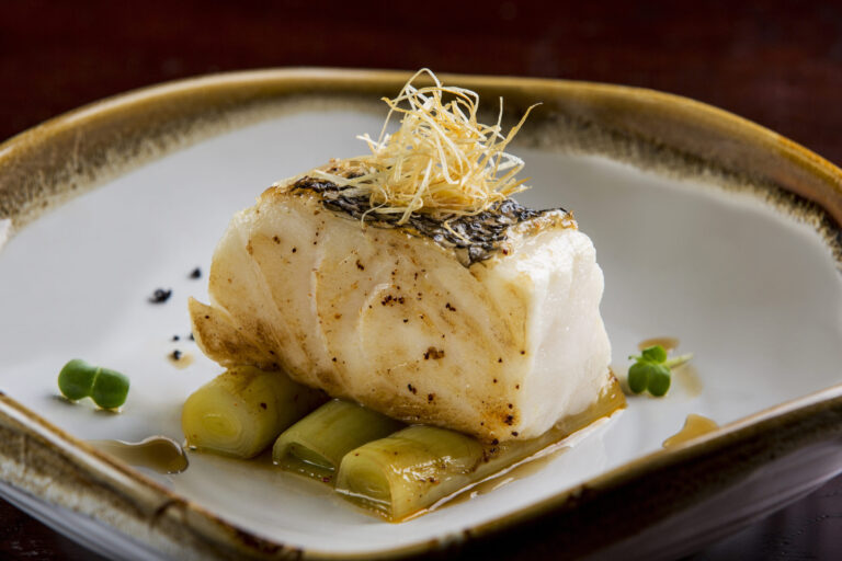 Grilled cod fillet on braised leeks, garnished with crispy shallots.