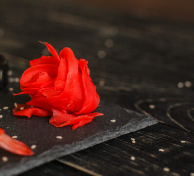 Rote Rose als Sushi auf schwarzer Schieferplatte auf schwarzem Hintergrund