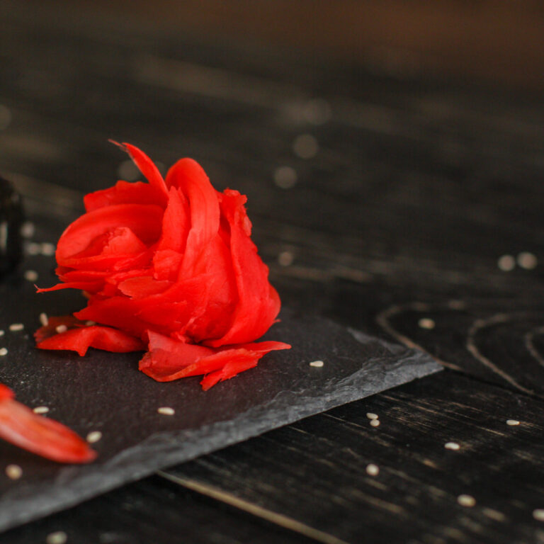 Rote Rose als Sushi auf schwarzer Schieferplatte auf schwarzem Hintergrund