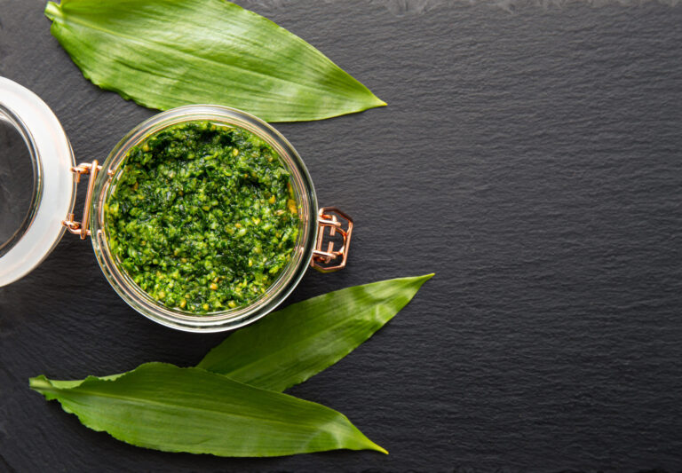 Homemade pesto sauce made with Allium ursinum leaves, known as wild garlic, ramsons, buckrams, broad-leaved garlic, wood garlic, bear leek or bear's garlic. Lot of copy space on black stone texture.